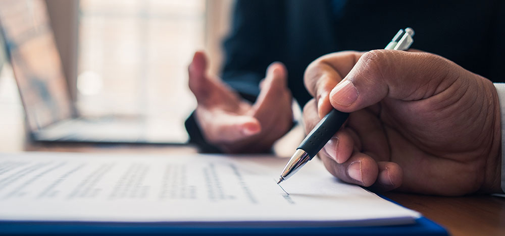 Hand holding pen, signing document.